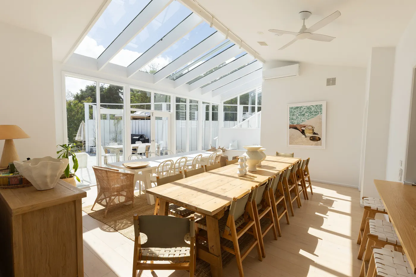 A long timber dining table under a glass roof, full of afternoon light