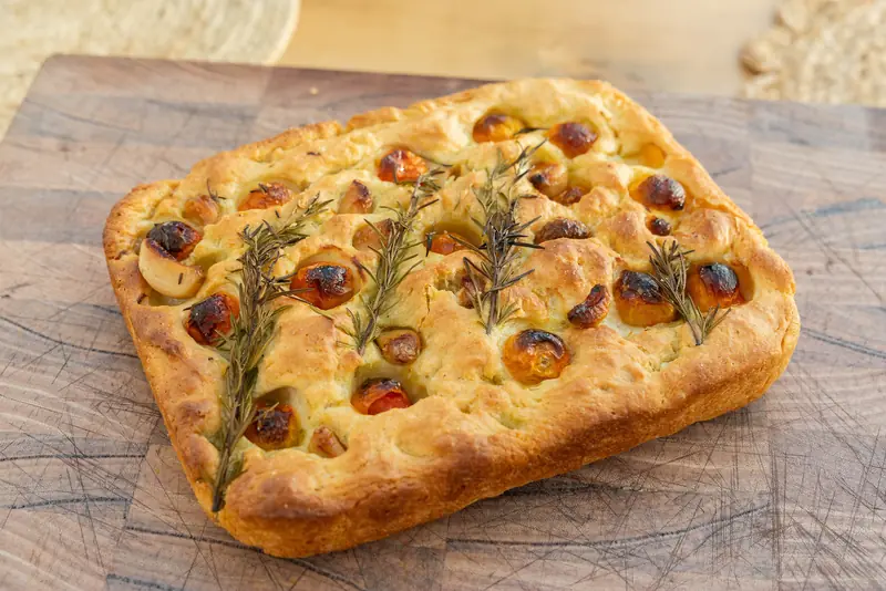 A tray of focaccia with rosemary and tomatoes