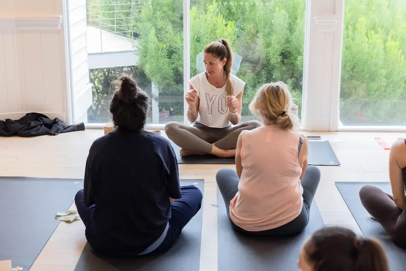 Guests sitting cross-legged, facing the yoga teacher