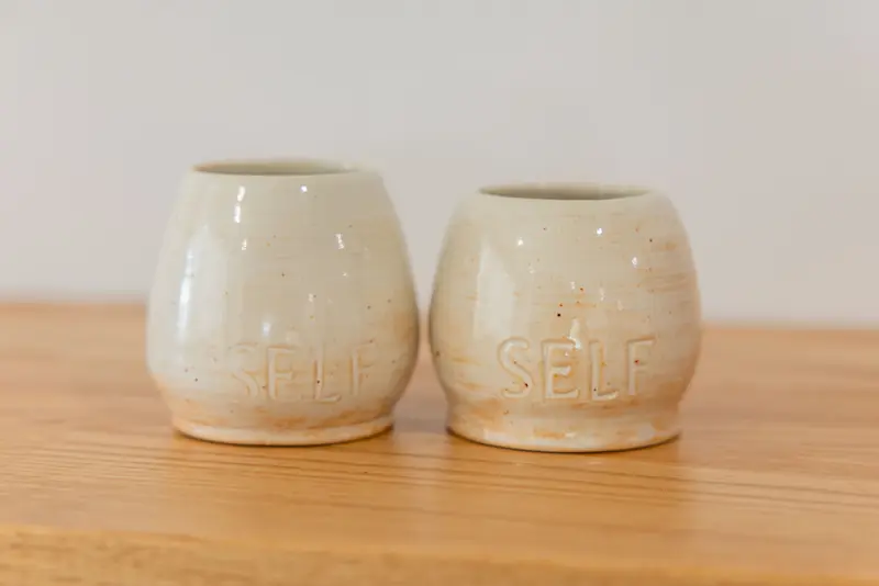 Two handmade cups stamped SELF on a timber table