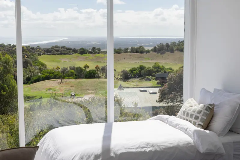 A bed beside a wide window over green paddocks