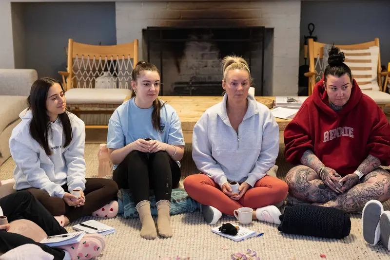 Guests sitting in the circle by the fireplace, cups in hand