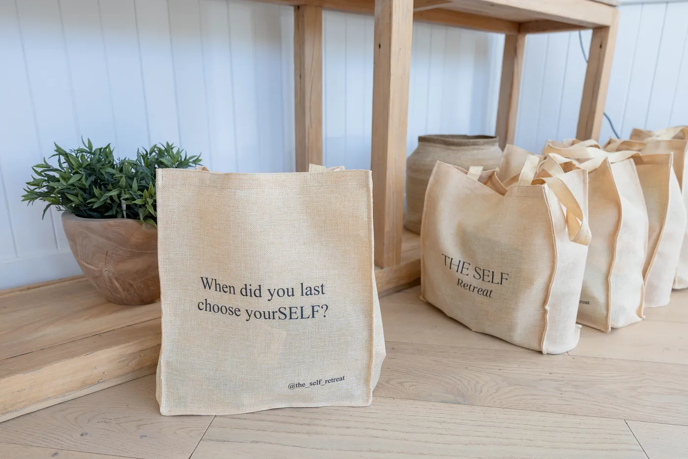 A row of canvas gift bags, the first printed with “When did you last choose yourSELF?”
