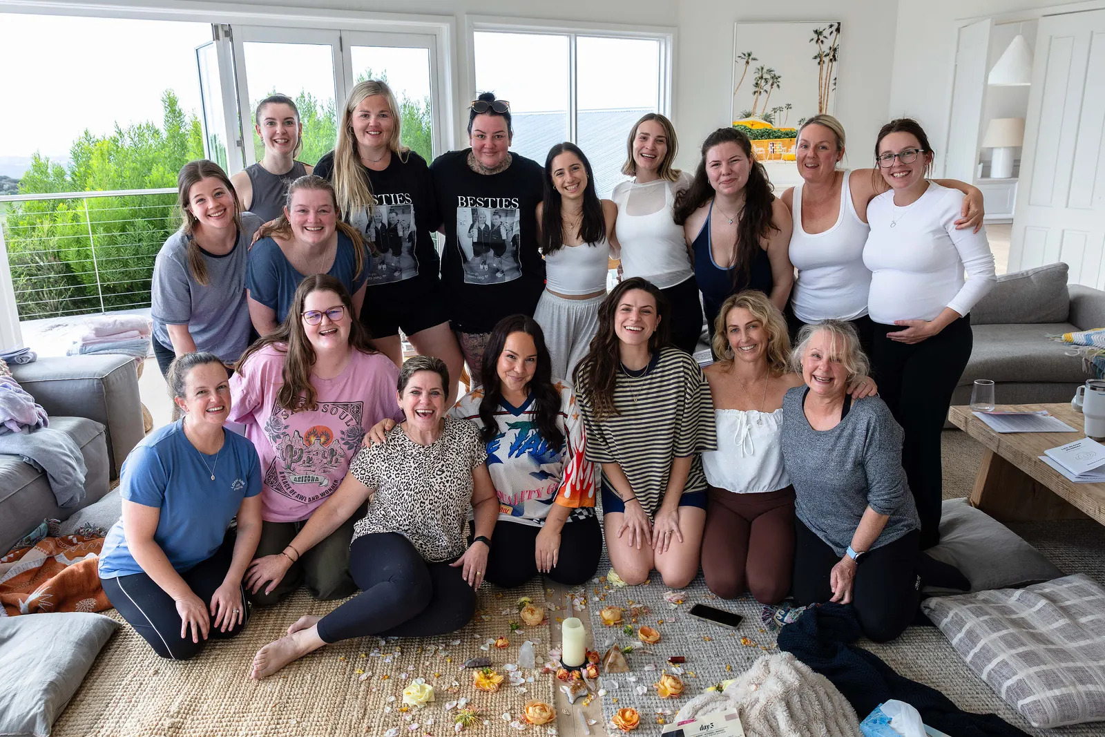 The March 2026 guests together on the lounge-room floor, smiling, with petals and a candle in front of them