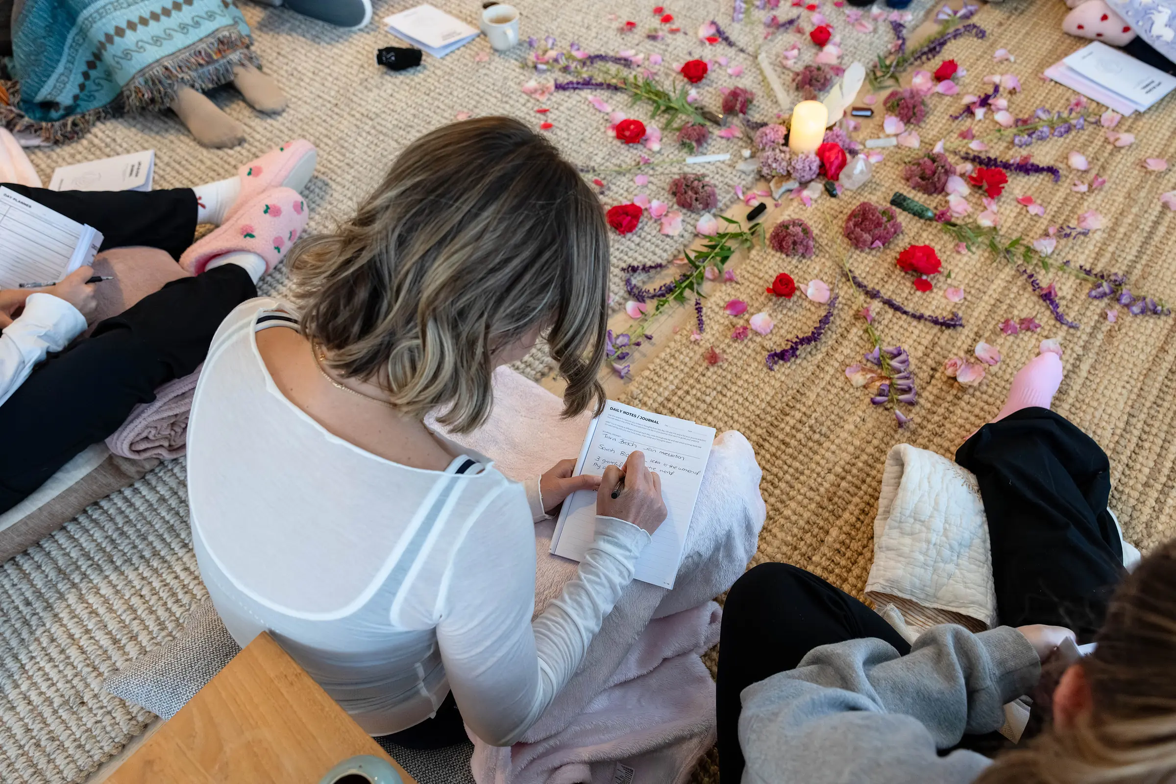 Sarah writing in her journal on the rug, among the roses, petals and candles of the circle