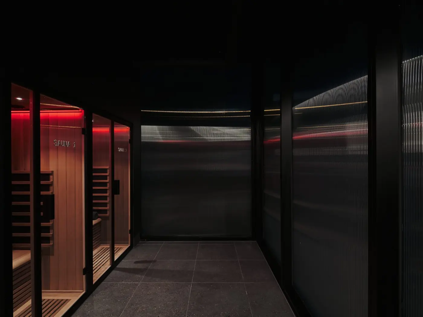 The corridor of glass-fronted saunas, lit in red