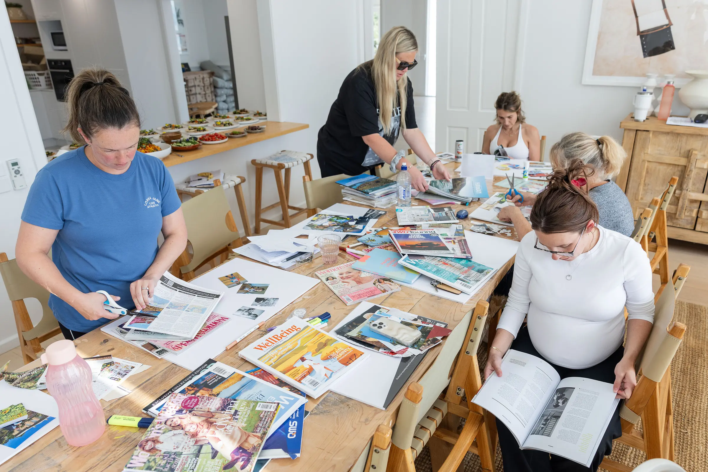 Guests around a long table covered in magazines and workbooks, making their vision boards
