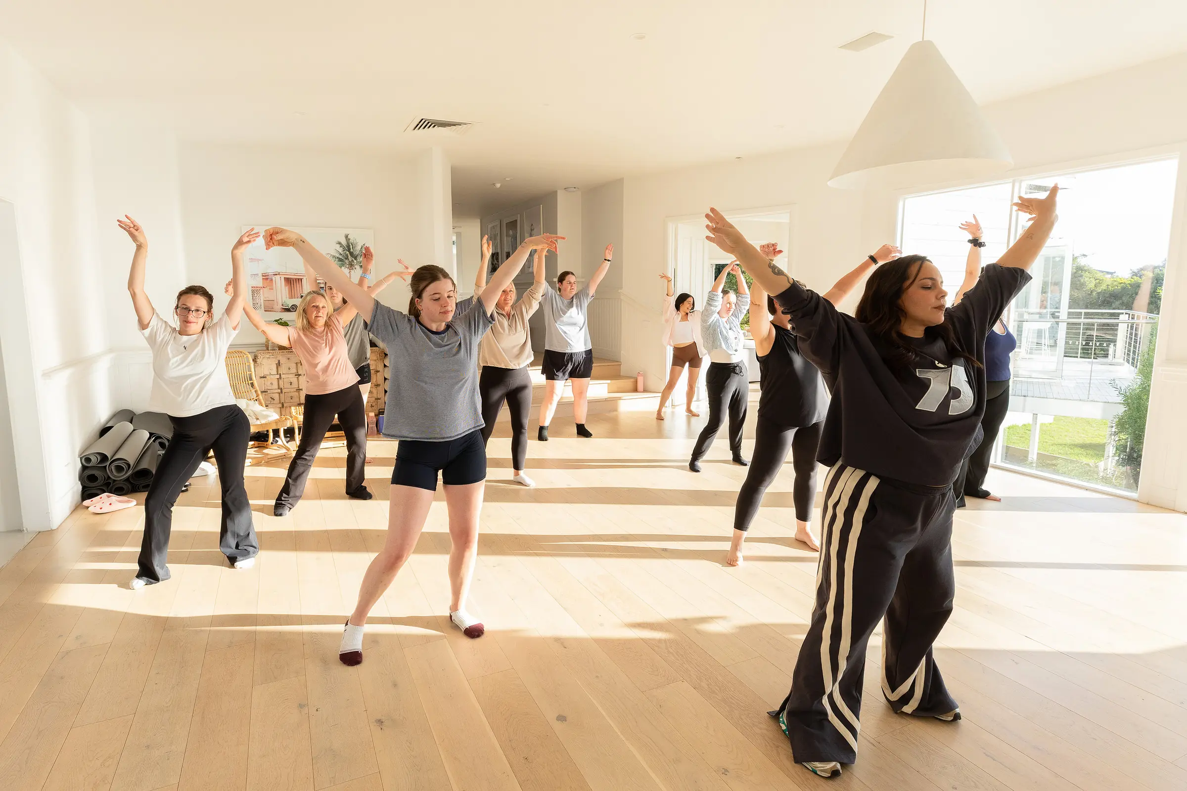 A dance class in full swing in the sunlit studio, arms in the air