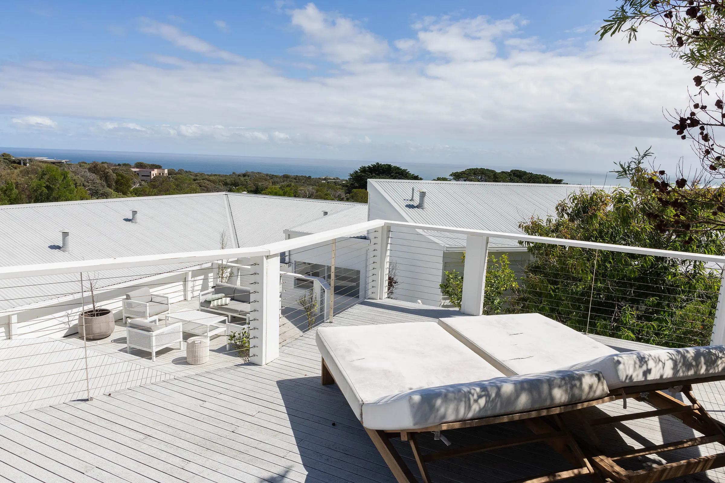 The Cape Retreat's white deck and daybed, looking over the tea-trees to the ocean