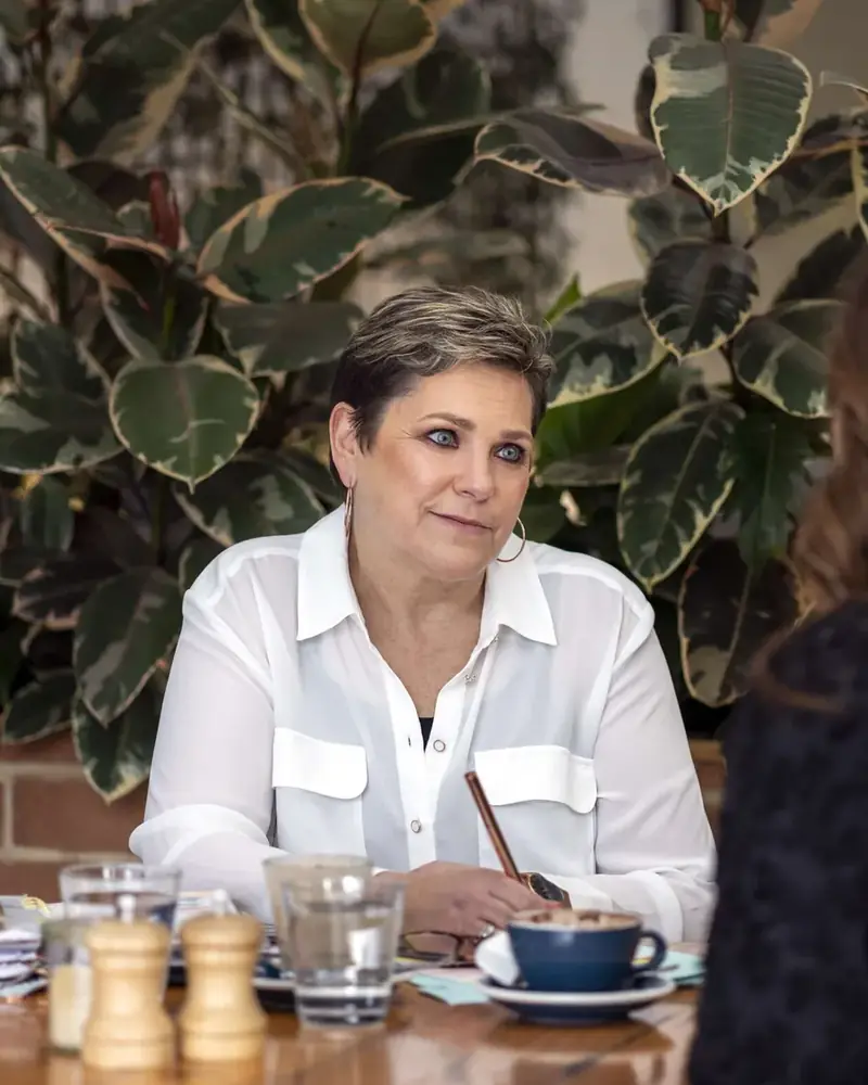 Sue in a white shirt, coaching across a café table
