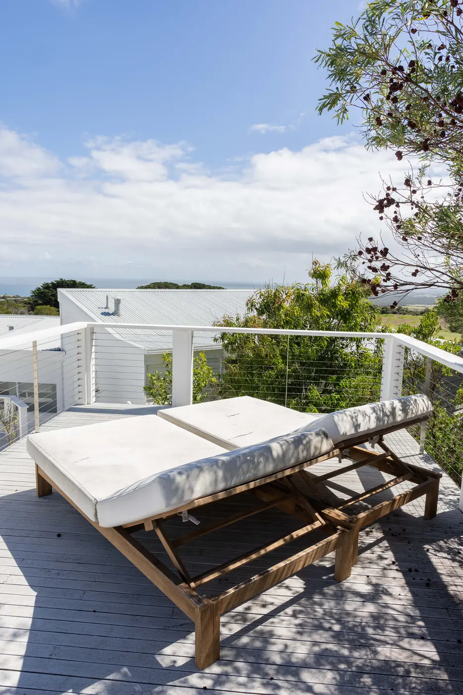 A timber daybed on the deck among the tea-trees