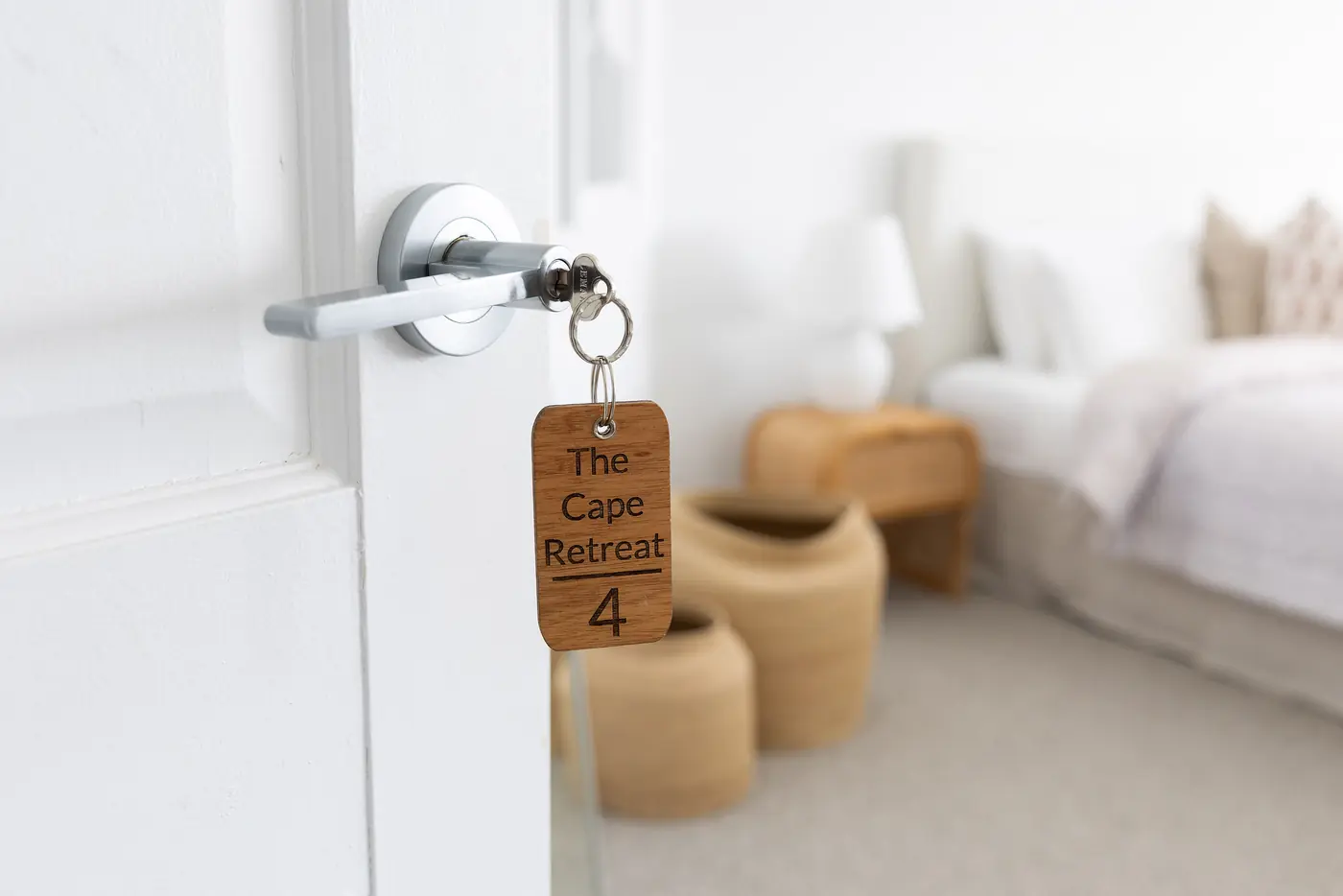 A room key on a timber tag reading The Cape Retreat, in the door of a white bedroom