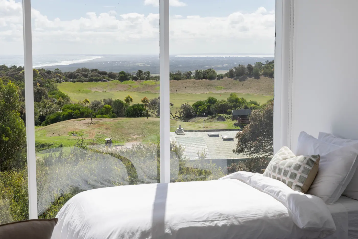 A bed beside a wide window over green paddocks