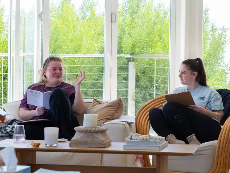 Two guests talking in the sunroom, workbooks in hand