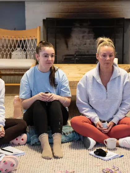 Two guests sitting in the circle by the fireplace, cups in hand